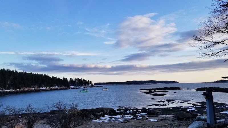 Milbridge shoreline along Acadia National Park features rocky coast, calm blue water, and boats at dusk.
