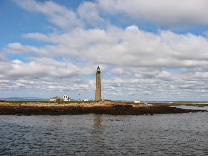 Milbridge Lighthouse stands on a rocky spit in Acadia National Park, with a white keeper's house nearby and calm harbor waters.
