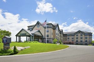 Lodge-style hotel with beige exterior, green porte-cochère, flagpole, and manicured lawn at Acadia National Park.