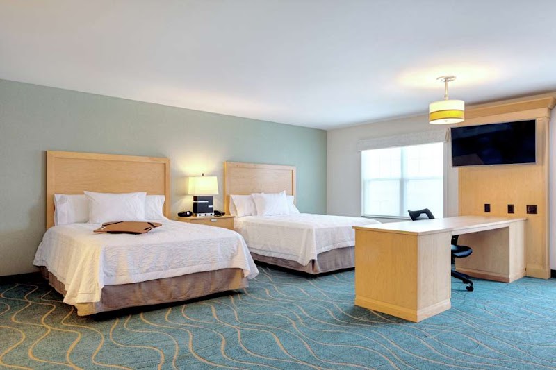 Two queen beds with white bedding, a wooden desk, wall-mounted TV, and a window in a bright Acadia National Park hotel room.