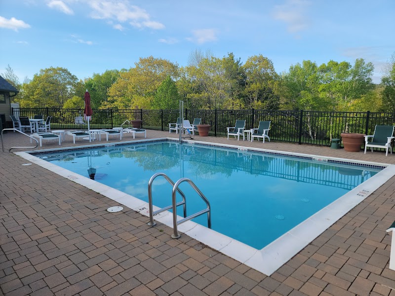 Outdoor pool with a metal ladder, brick deck, and white lounge chairs, Acadia National Park backdrop.