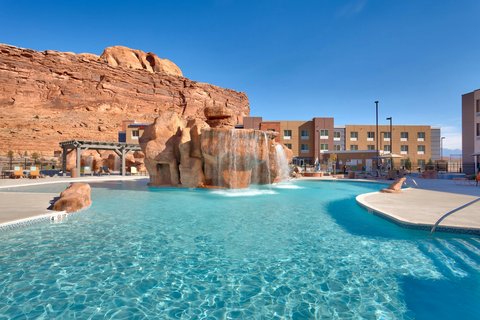 Resort pool with a rock waterfall and turquoise water, flanked by stucco buildings near Arches National Park.