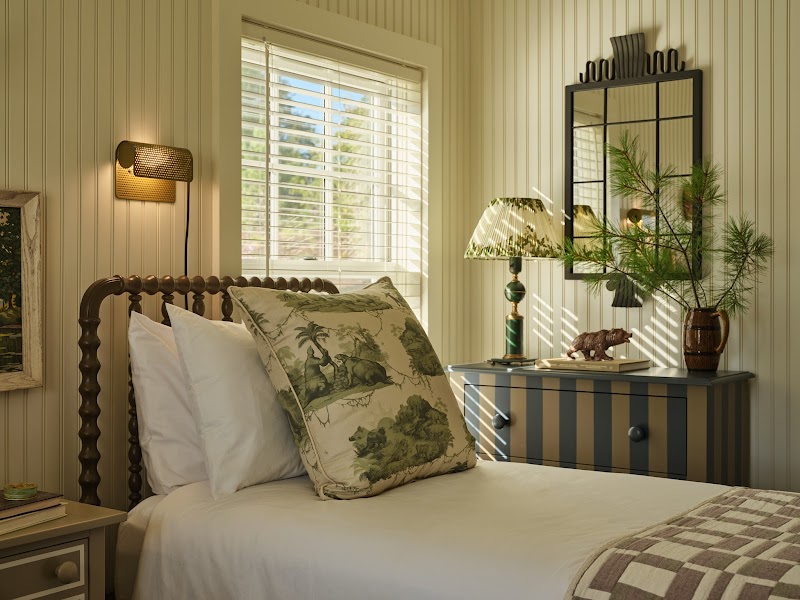 Cozy guest room at Asticou Hotel in Acadia National Park, featuring a striped dresser, botanical pillows, and sunlit window.