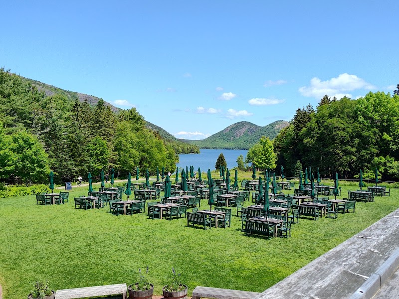 Outdoor seating on a grassy lawn overlooking Jordan Pond and surrounding trees at Acadia National Park in summer.