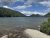 Jordan Pond shoreline at Acadia National Park with clear water, granite shore, and pine-covered hills under a blue sky.