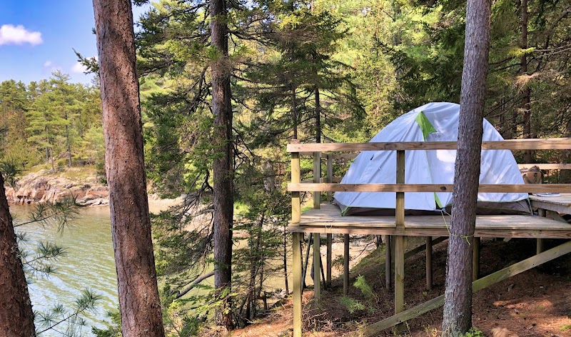 Tent on a wooden elevated platform among pines above a calm lake, with a gray tent nearby, in Acadia National Park.