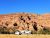 Blue sky over red sandstone cliffs in Arches National Park, with a campground row of campers and trees.