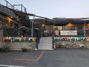 Exterior view of a seaside dining spot in Acadia National Park, decorated with colorful buoys along the railing and wooden buildings.