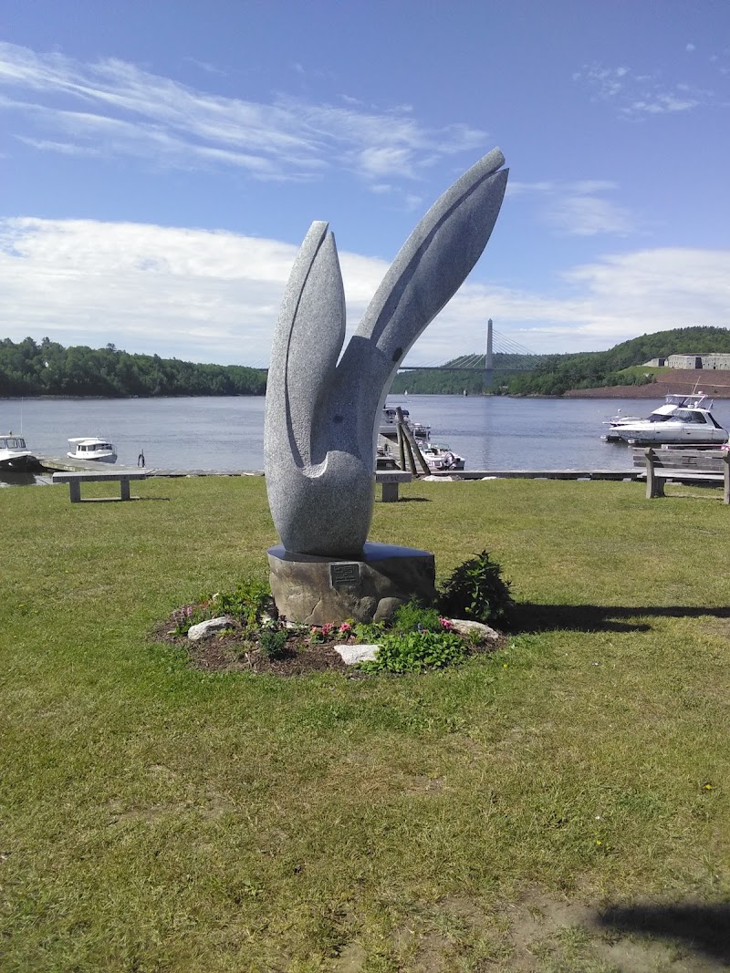 Bucksport waterfront sculpture along the Acadia National Park coast, with boats and a distant bridge.