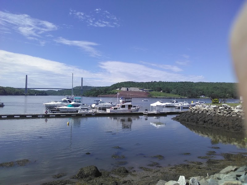 Bucksport marina in Acadia National Park with boats moored along the waterfront and a distant bridge under blue skies.