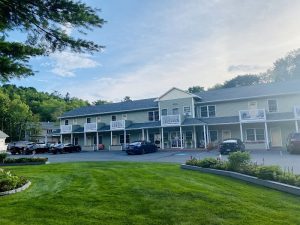Motel-style buildings with white balconies overlook a parking lot and green lawn in Acadia National Park.