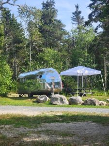 Shiny vintage camper beside a white canopy and picnic table at Reach Knolls campground, Acadia National Park.