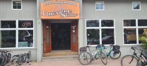 Open bicycle shop with an orange sign above double doors, several bikes parked on a brick sidewalk in Acadia National Park.