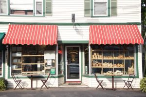 Bread displayed in window shelves under red striped awnings, white building facade with outdoor tables in Acadia National Park.
