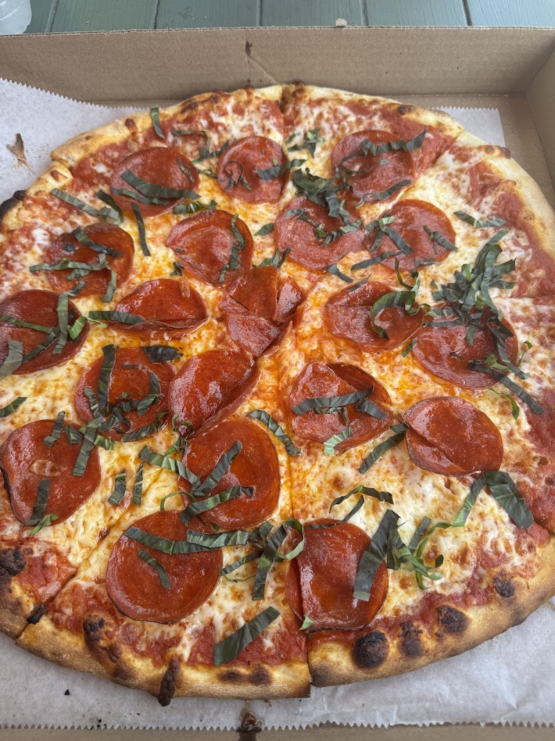Pepperoni pizza with melted cheese and scattered basil leaves on a golden crust inside a pizza box at Acadia National Park.