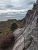 Steep granite trail with metal rungs climbs along a cliff at Acadia National Park, overlooking colorful autumn forest and the distant sea.