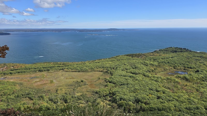 Overlook from Acadia National Park's Precipice Trailhead, blue Atlantic beyond green cliffs and distant islands.