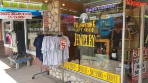 Yellowstone National Park gift shop storefront with bright signage, clothing racks outside, and souvenir displays.