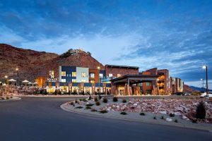 Hotel near Arches National Park with blue-gray facade, red rock hills, circular driveway, and twilight lighting.