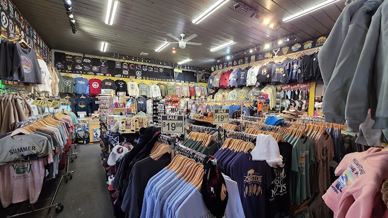 Inside a crowded souvenir shop in Yellowstone National Park, racks of colorful T-shirts, hats, and sale signs fill the space.