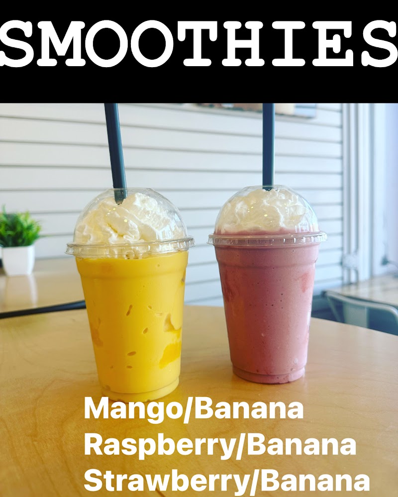 Two smoothies with whipped cream and blue straws, yellow and pink, on a wooden table inside Yellowstone National Park cafe.