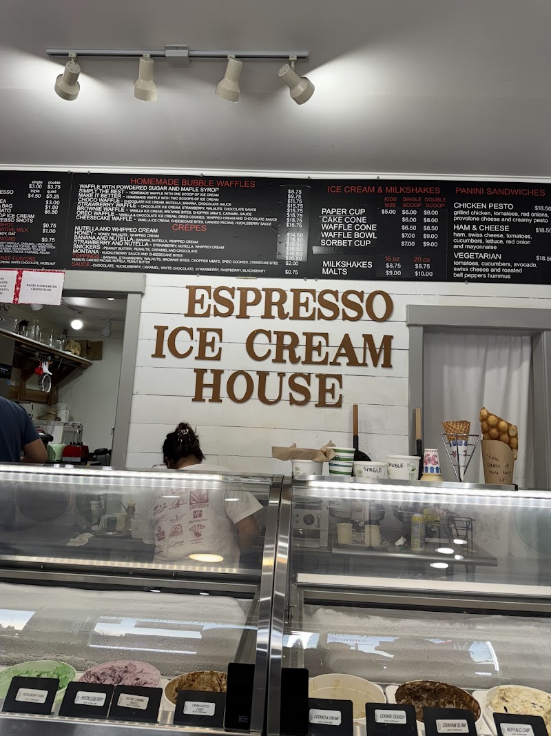Inside a Yellowstone National Park cafe counter with a white wall, a brown sign, glass ice cream display, and overhead menus.