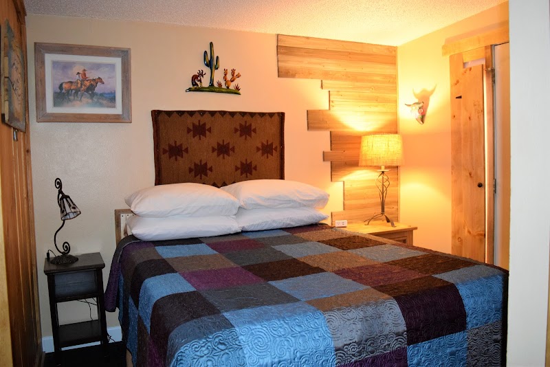 Cozy bedroom with patchwork quilt and two pillows, rustic wood paneling, cactus decor, and warm lamp light near Arches NP.