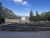 Outdoor amphitheater with wooden benches and a blank screen at a Yellowstone information station site, surrounded by pines and mountains.