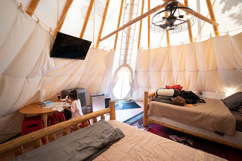 Interior of a canvas glamping tent in Arches NP: twin beds, circular window, ceiling fan, desk with a child drawing.