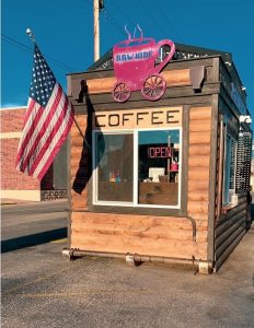 Yellowstone National Park coffee stand with an American flag and a pink wagon sign on a wood-clad storefront.