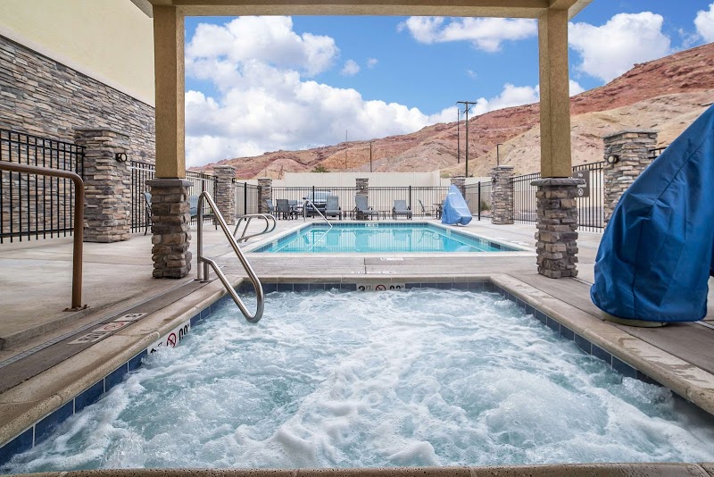 Outdoor pool with a bubbling hot tub under a shaded pavilion, desert hills and blue sky in Arches National Park.