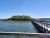 A wooden boardwalk extends over a calm glacier lake toward a shrub-covered island in Glacier National Park.