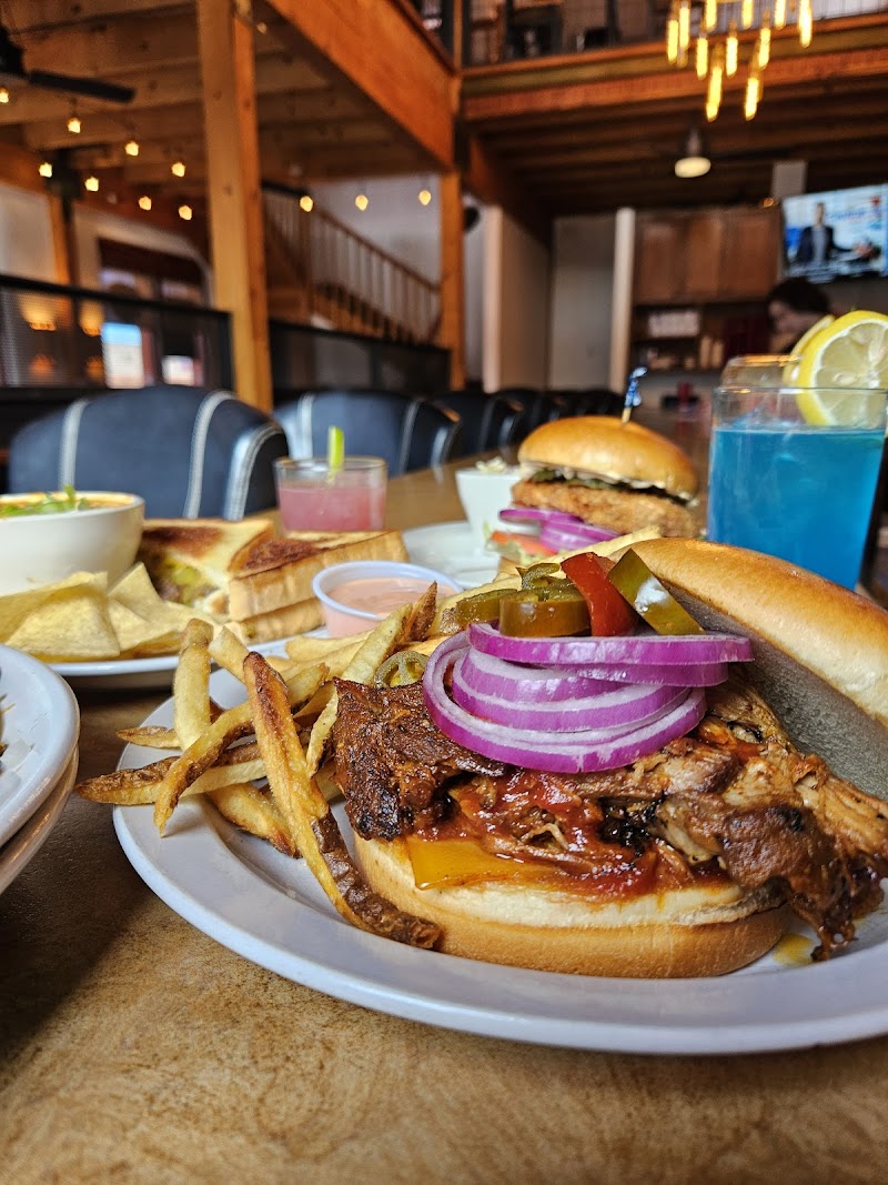 Inside a rustic restaurant at Arches National Park, a plate holds a loaded sandwich with onions, pickles, and fries.