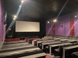 Interior of a theater-style dining space in Acadia National Park with a large screen, purple walls, red curtains, and rows of gray-topped tables and seats.