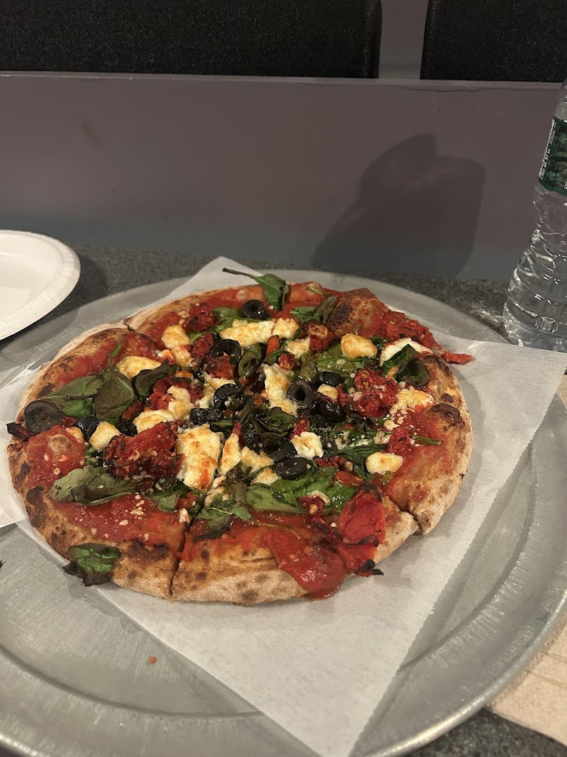 Pizza topped with spinach, olives, tomatoes and cheese on a crust beside a water bottle in Acadia National Park.