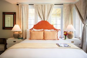 Cozy guest room at Acadia National Park lodging with coral headboard and striped pillows in a bright, inviting setting.