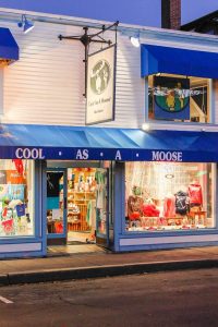 Blue-awning gift shop storefront with large window displays of clothing and souvenirs in Acadia National Park.