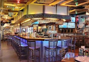 Cozy bar interior with a curved counter, metal stools, hanging glassware, and chalkboard menus in Acadia National Park.