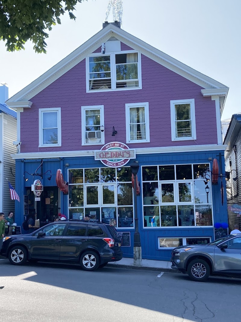 Two-story pink building with white trim and blue storefront, large windows, sign, and parked cars in Acadia National Park.