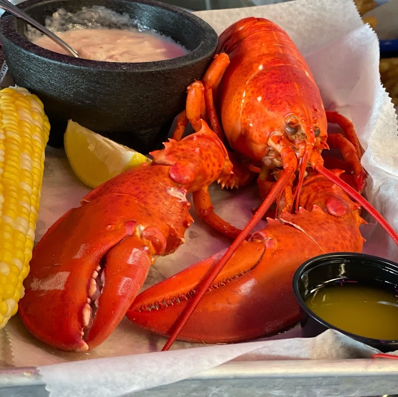 Bright orange lobster claws and tail with corn on the cob, lemon wedge, and dipping sauces in Acadia National Park restaurant setting.