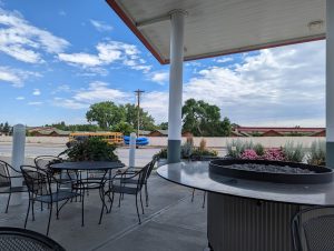 Outdoor seating area near a lodge in Yellowstone National Park, under a covered patio with a circular fire pit and blue sky.