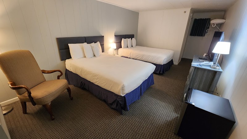 Two queen beds with white linens and navy bed skirts, a beige armchair, and a desk area in Acadia National Park lodge room.