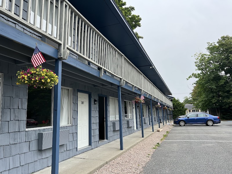 Blue motel row with white doors and a second-floor balcony, hanging flower baskets, flags, and a blue car in Acadia National Park.