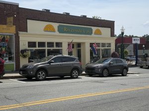 Cafe storefront along Main Street in Bar Harbor, Acadia National Park, with flags and parked cars.