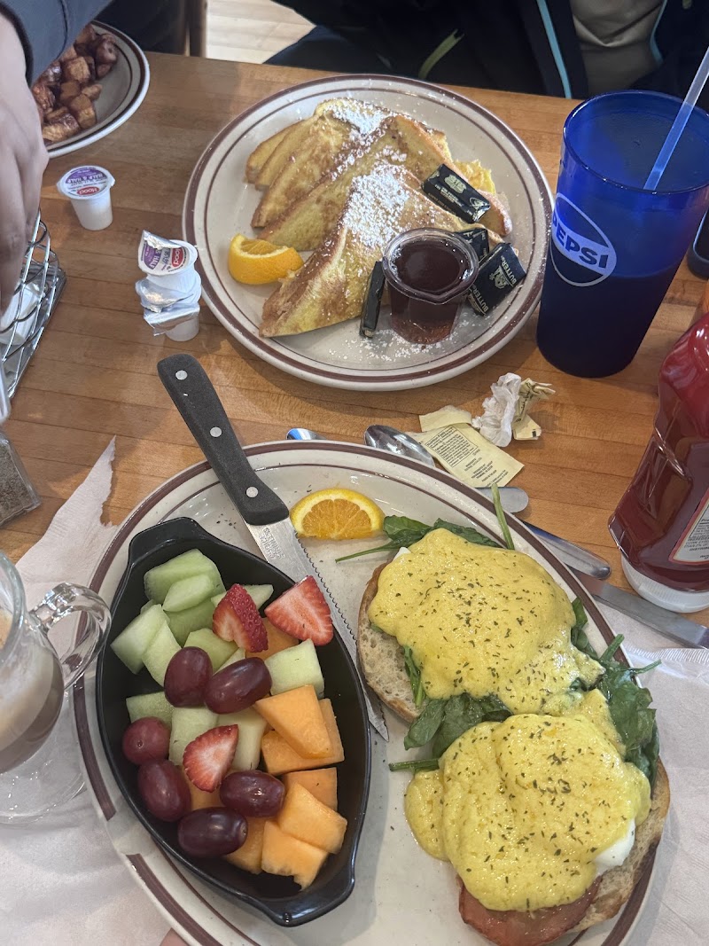 Two breakfast plates featuring eggs Benedict with hollandaise and greens plus French toast with powdered sugar, set at a cafe table in Acadia National Park.
