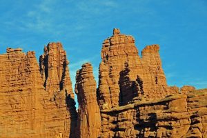 Tall red sandstone spires rise above a rocky foreground under a bright blue sky at Arches National Park.