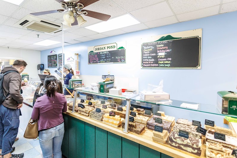 Visitors browse a glass display case filled with fudge and cakes inside a blue-walled gift shop at Acadia National Park.