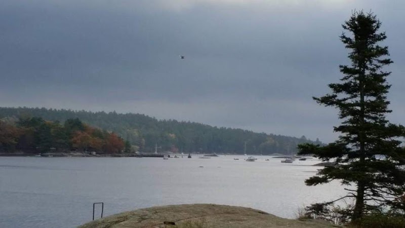 Blue Hill Harbor in Acadia National Park seen from a rocky overlook with boats on the calm water under a cloudy sky.