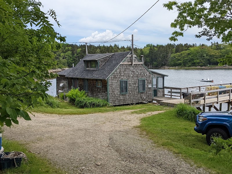 Brooksville waterfront cottage along Acadia National Park's rocky shore, with a wooden dock and a small boat nearby.
