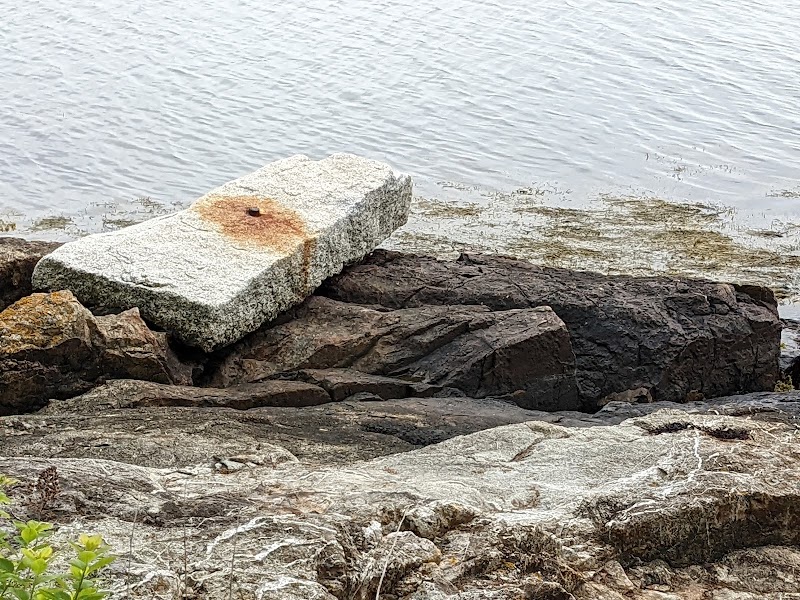 Brooksville shoreline along Acadia National Park, showing a weathered concrete block resting on layered rocks beside calm water.